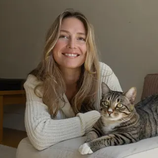 Maya, a caregiver, at home with a tabby cat resting beside her.