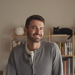 Daniel, a caregiver, in his living room with a black cat behind him.